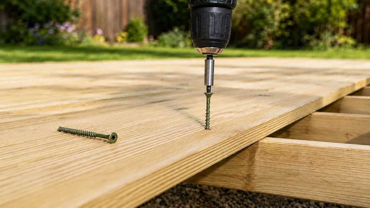 Green-coated decking screw being driven into pressure-treated timber decking beside a loose screw